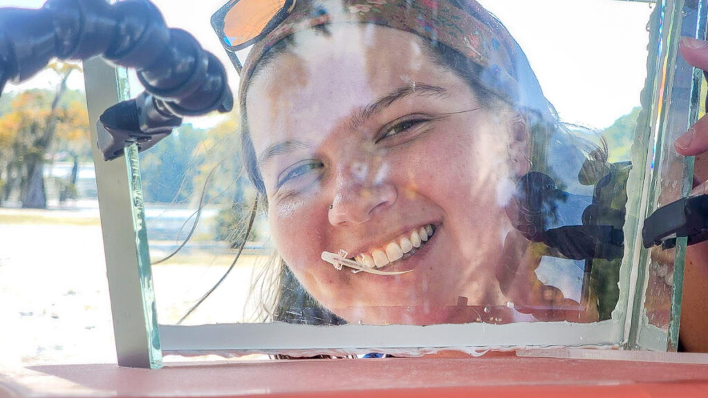 Gretchen Hilt smiling behind the glass that a collected Georgia Blind Cave Salamander is on.