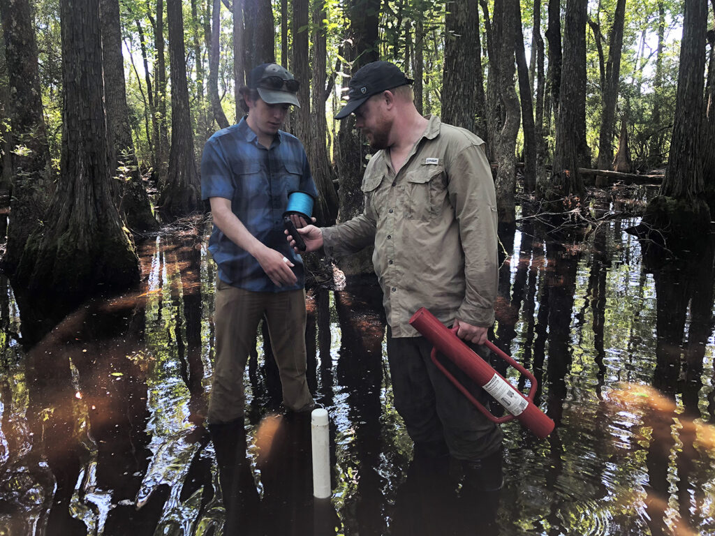 Justin Sanclemente and Ben Stegenga installing a hydrologic monitoring well at the center of a small wetland. – Houston Chandler